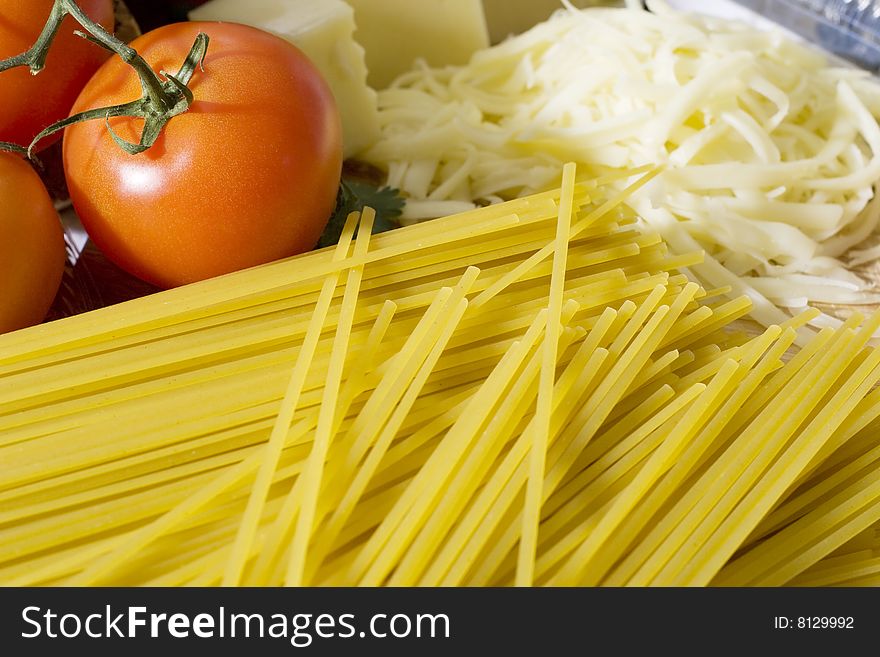 Overhead shot of raw spaghetti next to a tomatoes and grated cheese