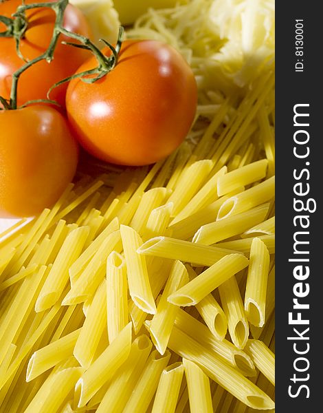 Overhead shot of raw spaghetti and macaroni next to a tomatoes and grated cheese