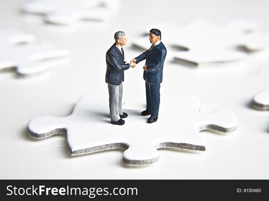 Businessman figurines shaking hands while standing on a puzzle pieces. Businessman figurines shaking hands while standing on a puzzle pieces