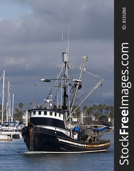 A black and white fishing boat leaving the harbor and dark storm clouds in the sky. A black and white fishing boat leaving the harbor and dark storm clouds in the sky.