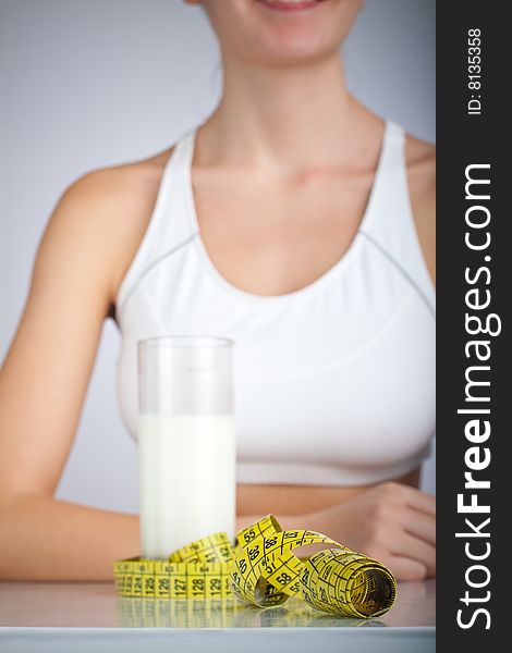 Glass filled with milk surrounded with measuring tape, smiling woman in the background. Glass filled with milk surrounded with measuring tape, smiling woman in the background