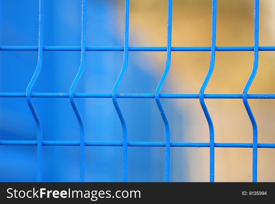 Close up of blue metal fence with blurred blue and orange background. Close up of blue metal fence with blurred blue and orange background