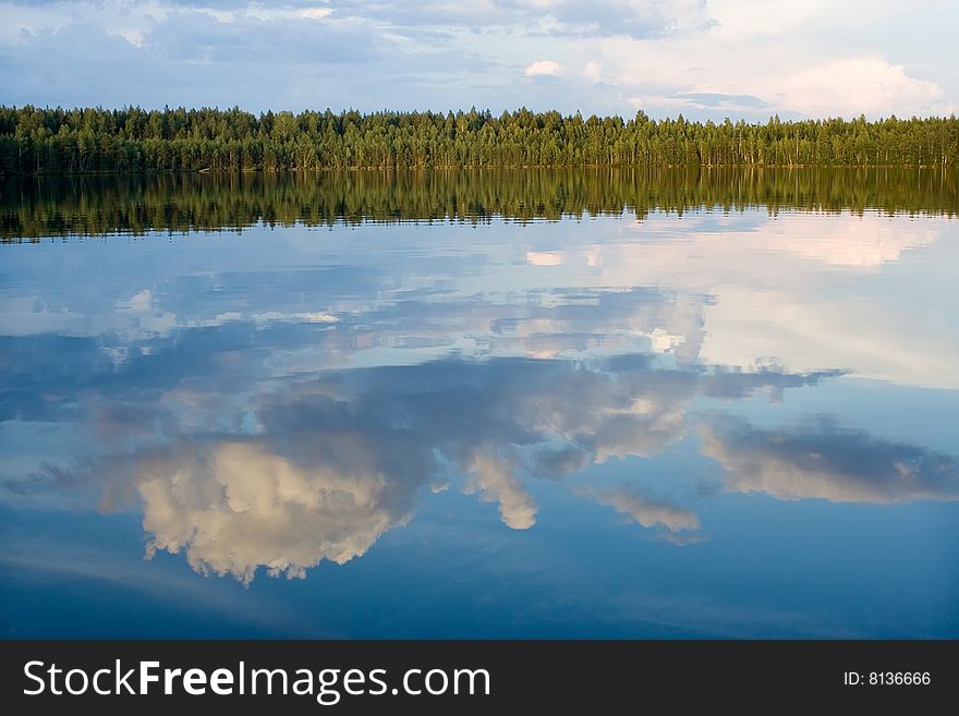 In lake in calm water is reflected wood and cloud. In lake in calm water is reflected wood and cloud