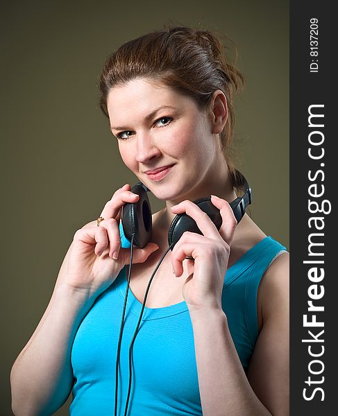 Beautiful Smiling Redhead Girl Wearing Music Headphones with blue tank top shirt holding around neck. Beautiful Smiling Redhead Girl Wearing Music Headphones with blue tank top shirt holding around neck