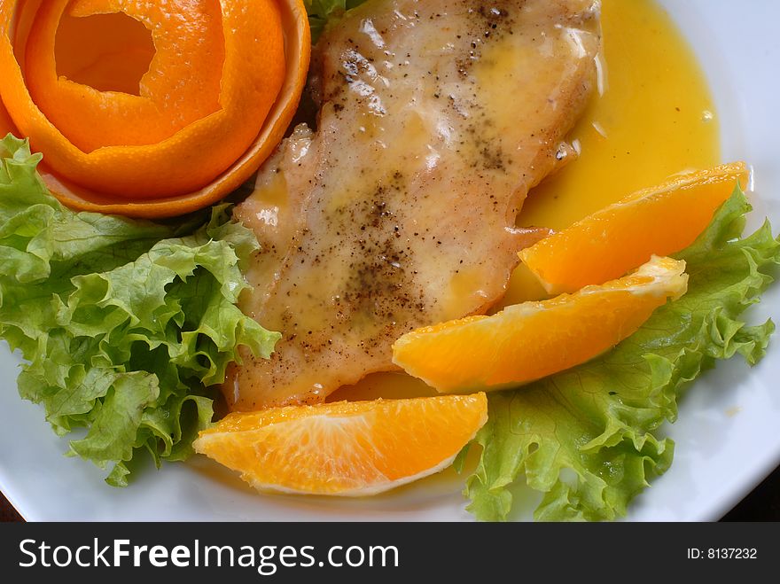 A plate of juicy pork chop with green salad, decorated with slices of orange and citron shaped as a rose. A plate of juicy pork chop with green salad, decorated with slices of orange and citron shaped as a rose