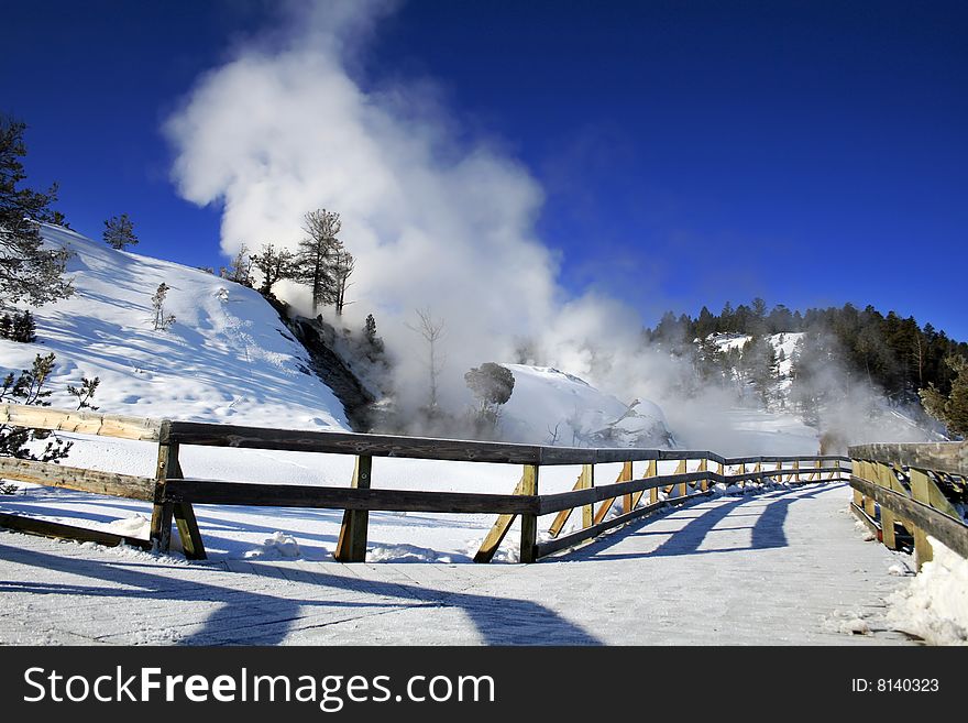 A walkway leads up to the travertine formations of Mammoth Hot Springs in Yellowstone National Park on a winter morning. A walkway leads up to the travertine formations of Mammoth Hot Springs in Yellowstone National Park on a winter morning.