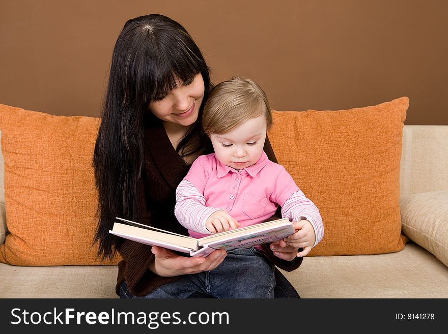 Mother and daughter reading book on sofa