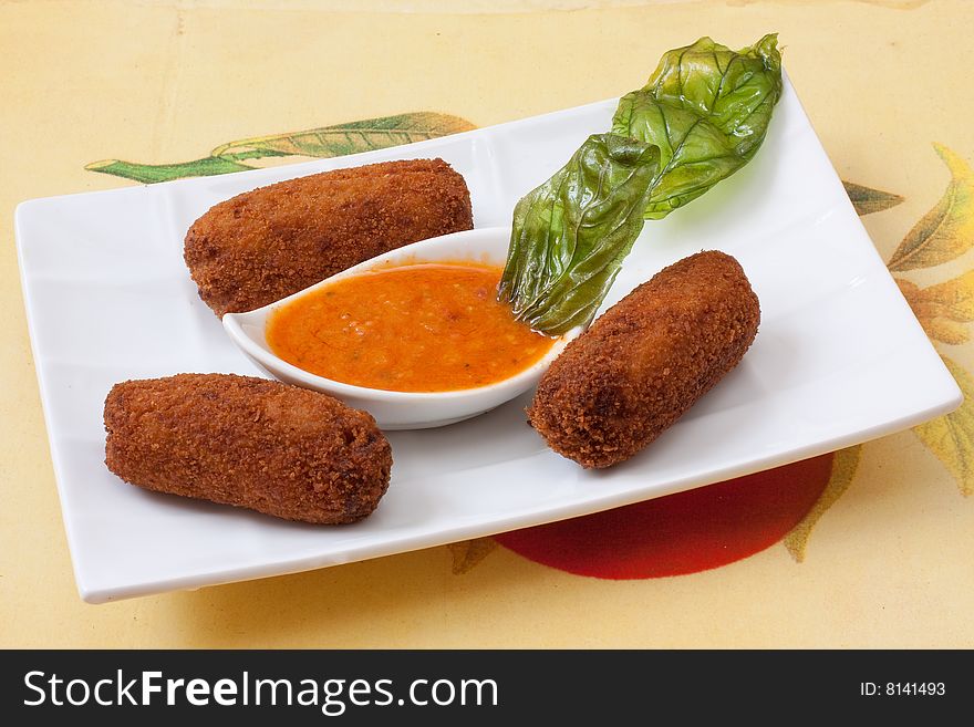 Chicken fried croquettes on white platter with basil leaf