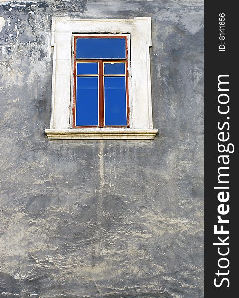 The wall of an old building with a window in which is reflected the  blue sky