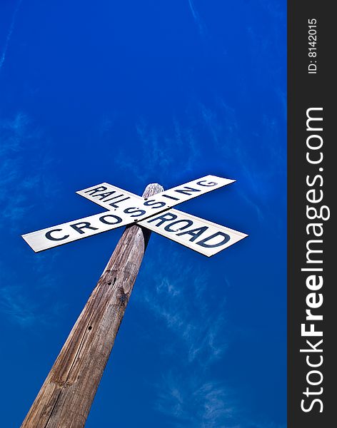 Looking up at a railroad crossing sign against the dark blue sky with a few lightly scattered clouds.