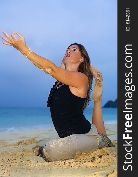 Young woman doing yoga at the beach in Hawaii at daybreak.