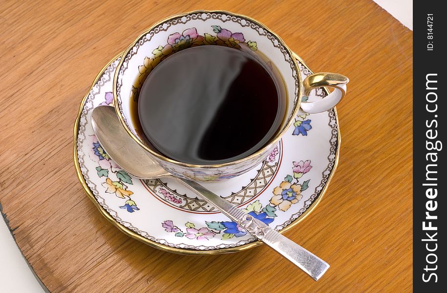 Coffee in an ornate china cup on a wood surface
