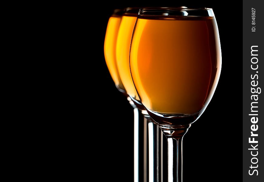 Three small glasses filled with orange liquor on black background. Three small glasses filled with orange liquor on black background