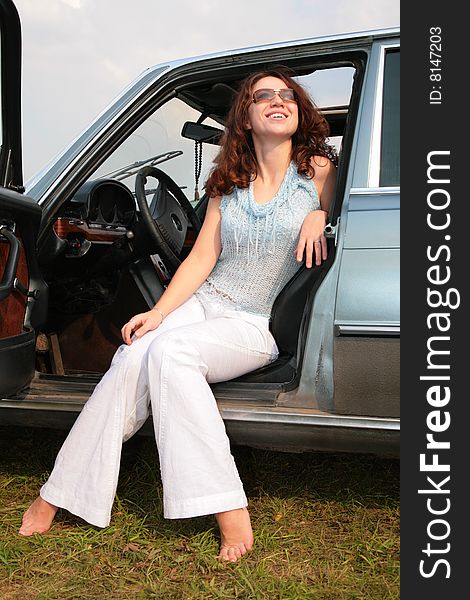 Woman sits in the car, having put bare feet on the ground