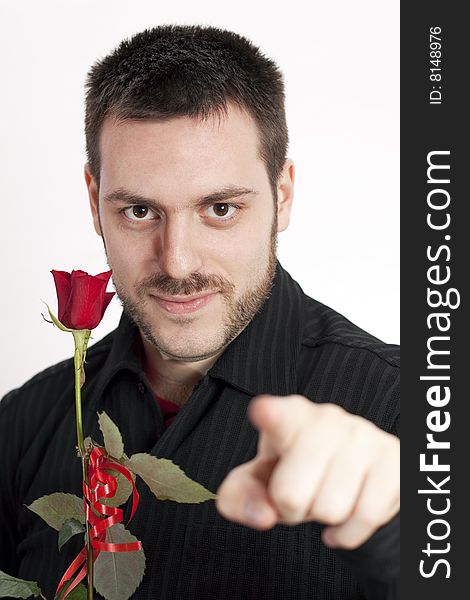 Young, handsome man, holding a red rose, pointing his finger and looking at the camera, smiling. Young, handsome man, holding a red rose, pointing his finger and looking at the camera, smiling