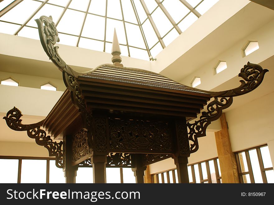 An Asian handcrafted gazebo rooftop under the glass rooftop of a shopping mall.