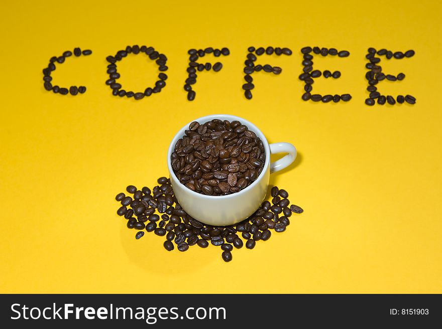 Coffee written with beans on yellow background.  Cup on foreground.