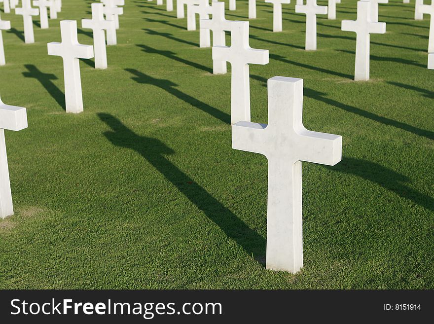 White marble crosses in a military cemetery casting their shadows on the grass