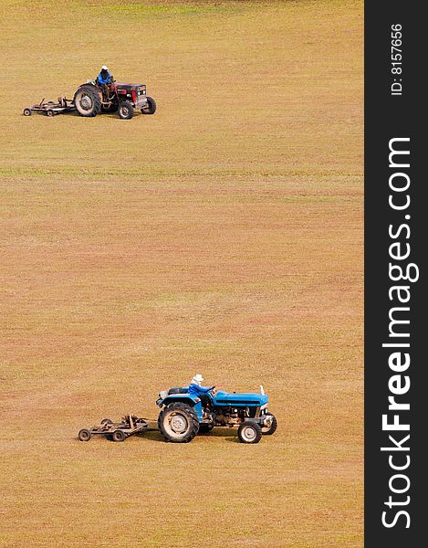 A pair of tractor-towed mowers moving a large open flat dry field. A pair of tractor-towed mowers moving a large open flat dry field