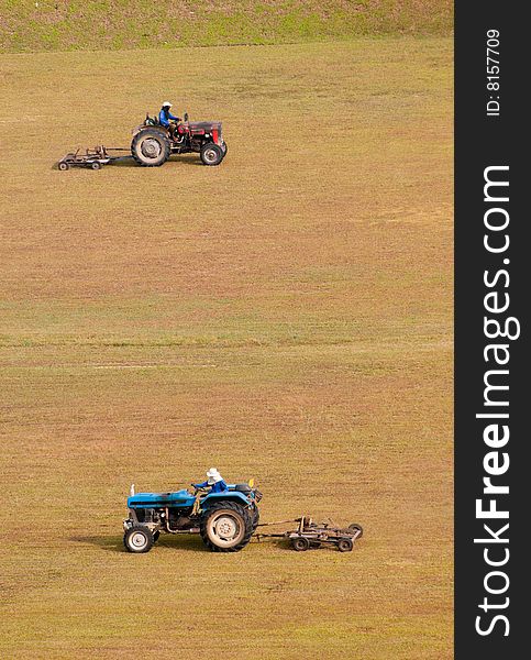 A pair of tractor-towed mowers moving a large open flat dry field. A pair of tractor-towed mowers moving a large open flat dry field