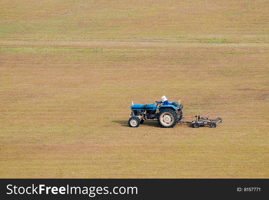 A tractor-towed mower moving a large open flat dry field