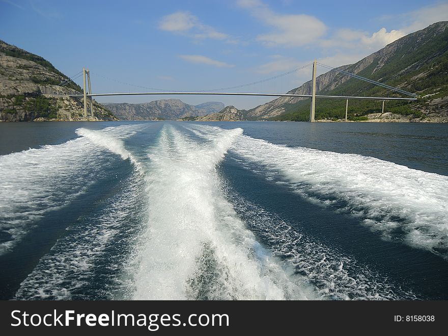 View of a bridge in a fjord in Norway from a boat with its wake