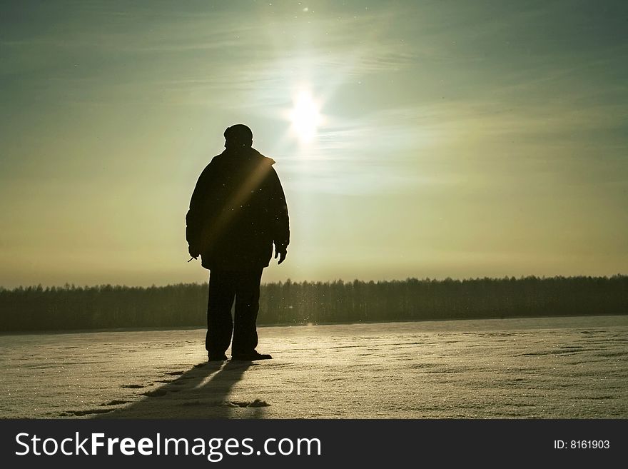 The person stands on a snow field under light of evening sun. The person stands on a snow field under light of evening sun