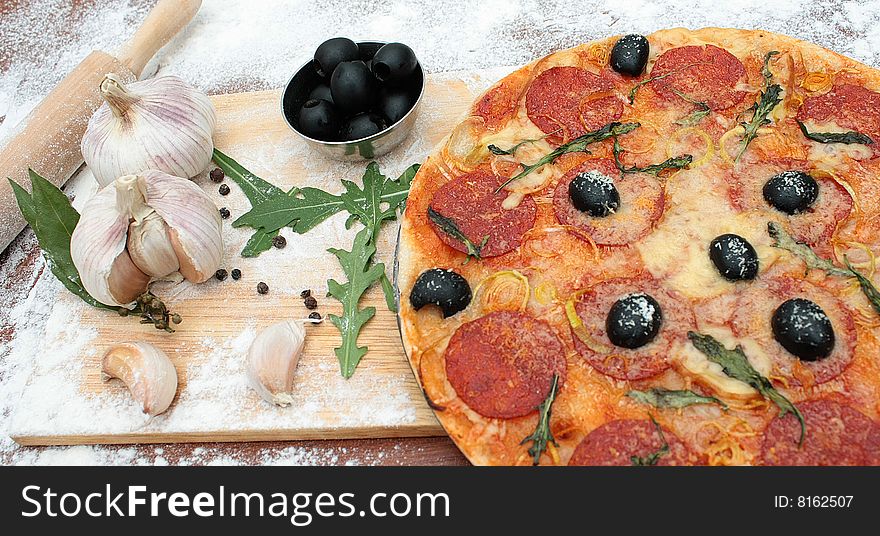 Ingredients of pizza. Pizza, olives, garlic, rolling pin, herbs and vegetables on the table. Ingredients of pizza. Pizza, olives, garlic, rolling pin, herbs and vegetables on the table