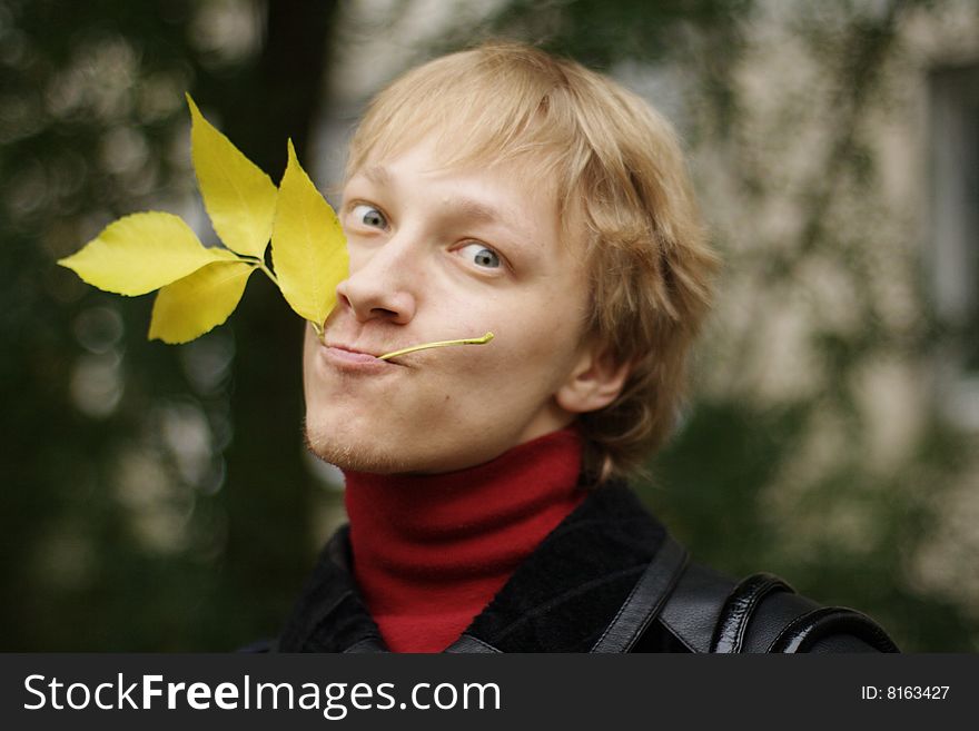 A young man with yellow autumn leaves in teeth