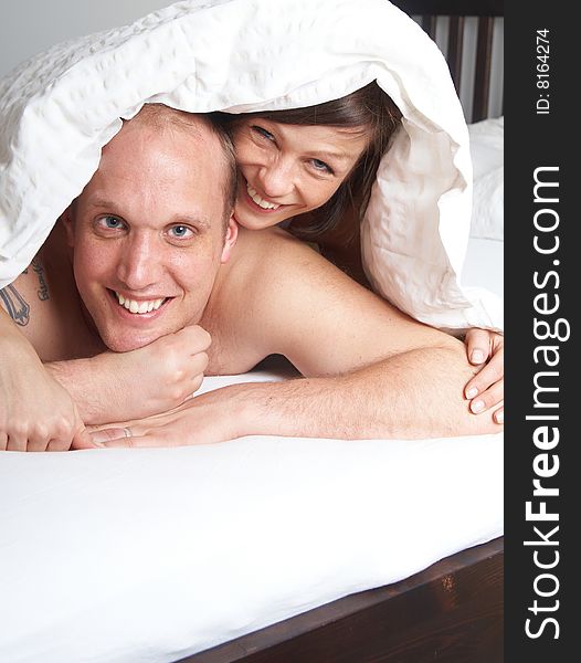 Young couple in their bed. They are playing in romance under the sheets.