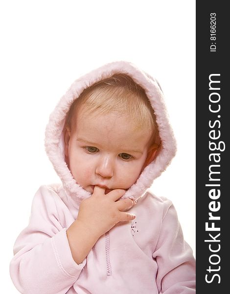 A cute baby in a pink jacket and hood finger in mouth looking down. A cute baby in a pink jacket and hood finger in mouth looking down