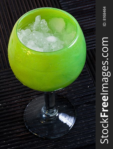 A frozen margarita in a decorative glass on a hardwood surface.