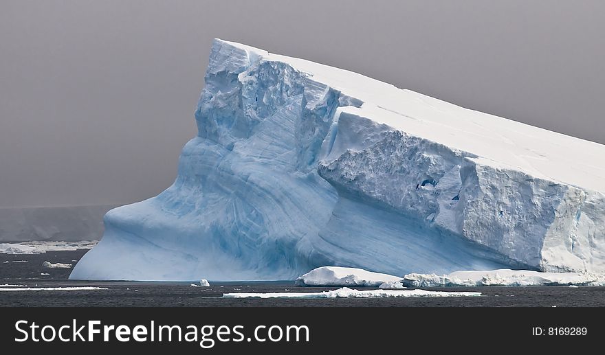 A huge tabular iceberg slanting into the sea in Antarctica. A huge tabular iceberg slanting into the sea in Antarctica.