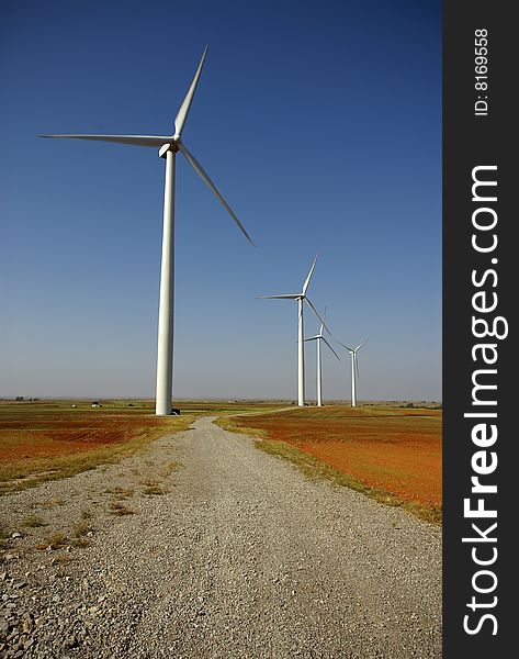 A service road winds between the wind turbines in a rural area. A service road winds between the wind turbines in a rural area.