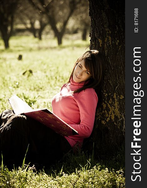Young cheerful woman enjoying a book in the forest.