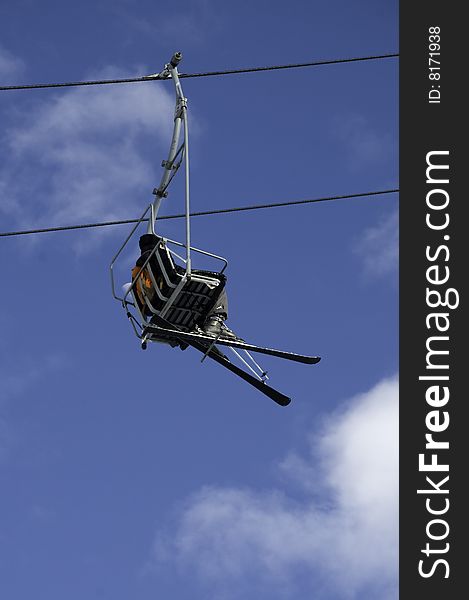 Seen from below a person with skis sitting in a chair lift against a blue sky