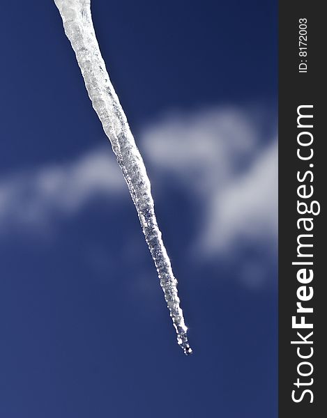 A single icicle against a blus sky and whispy cloud