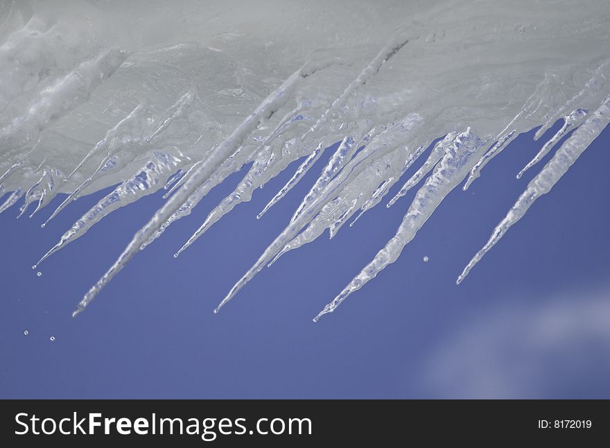 Icicles against a bright blue sky with drips of melting water