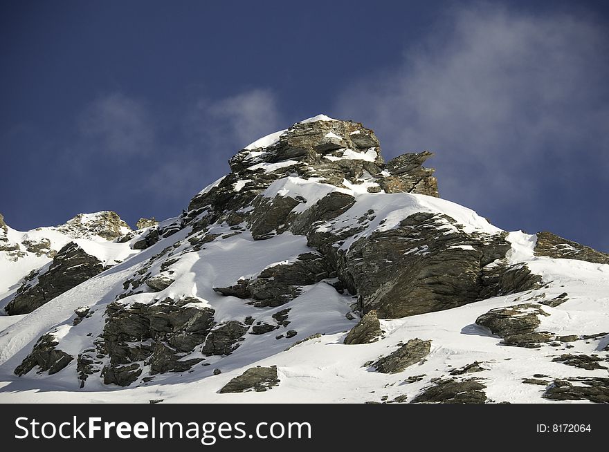 A snow covered rocky mountain top with blue sky