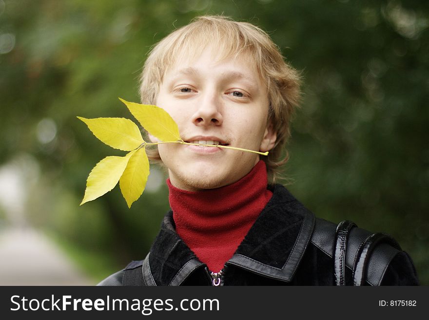 A young man with yellow autumn leaves in your teeth