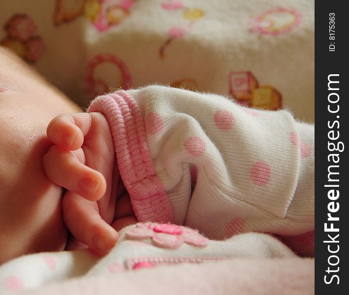 Newborn's fingers, in pink and white cotton outfit, touching face. Newborn's fingers, in pink and white cotton outfit, touching face