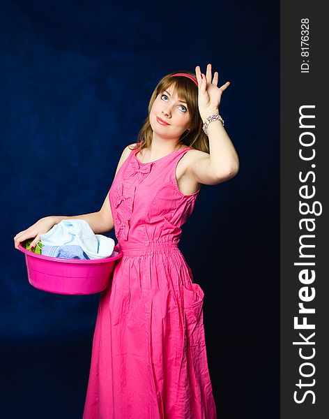 Charming young tired housewife with a basin full of clothes, against blue background