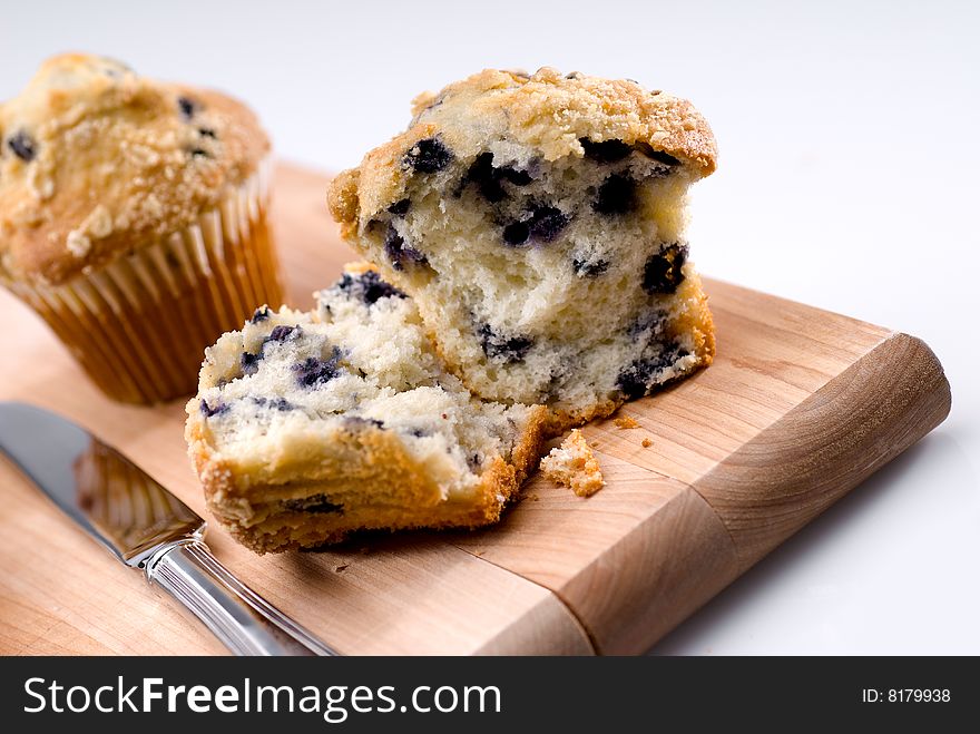 Two blueberry muffins on wood cutting board with knife. Two blueberry muffins on wood cutting board with knife