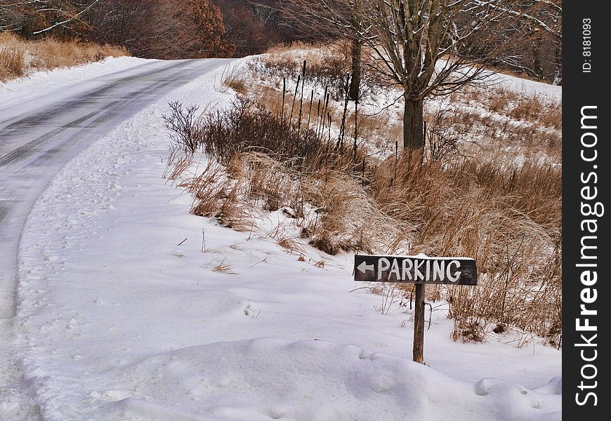 Wooden parking sign alongside a road in a park after a snowfall.
