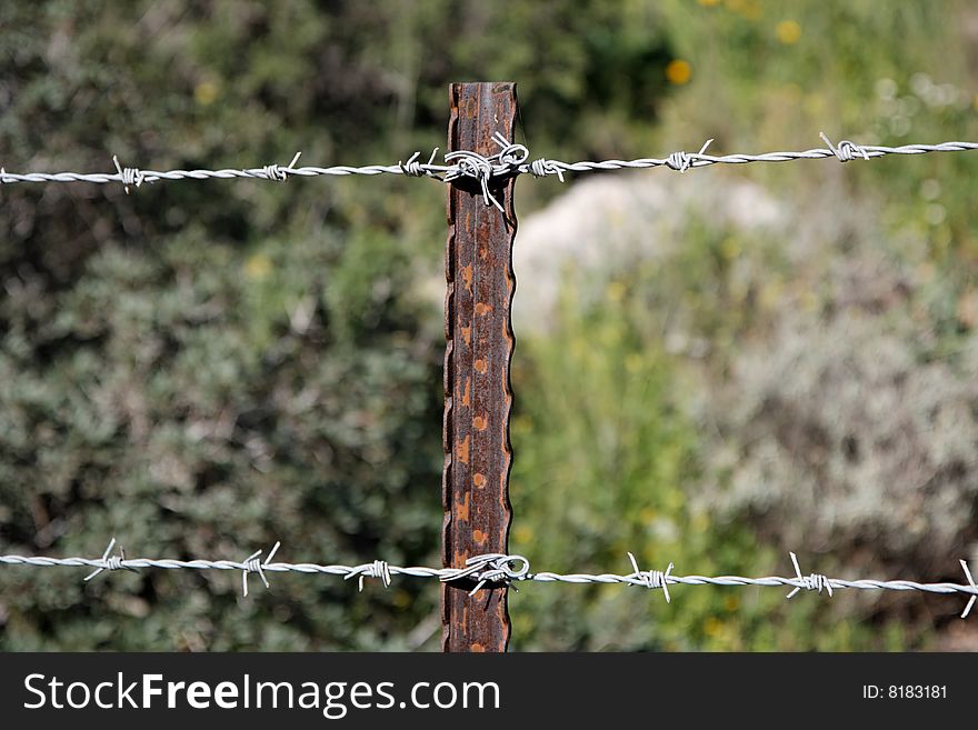 Two strands of barbed wire fence on the rusty steel post