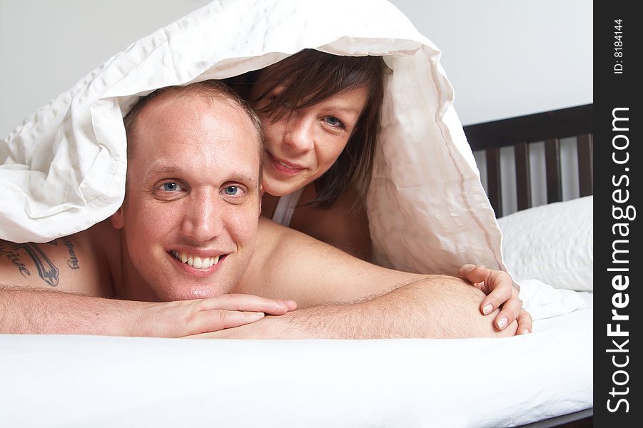 Young couple in their bed. They are playing in romance under the sheets. Young couple in their bed. They are playing in romance under the sheets.