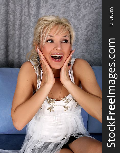 Young lovely blond girl in surprise emotions in sofa in room