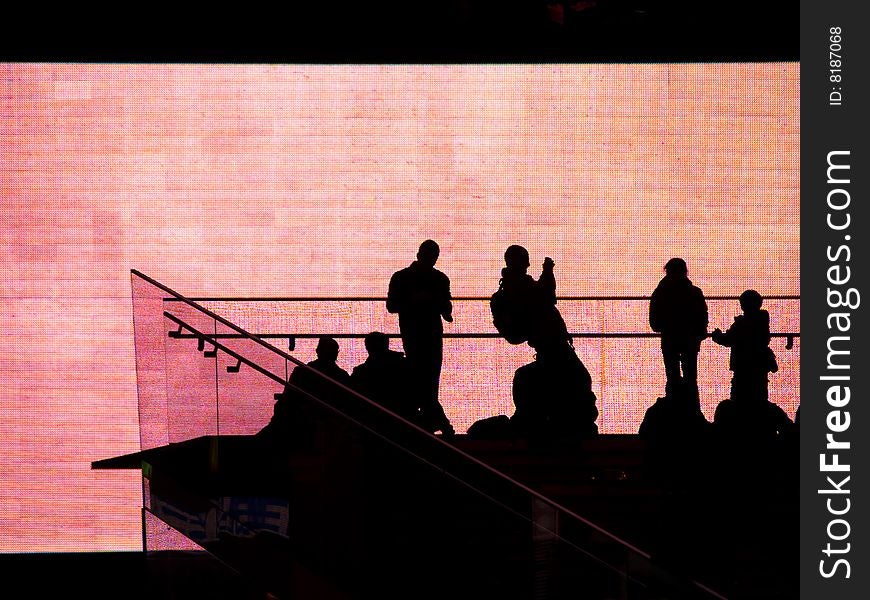 People silhouetted against huge video screen.