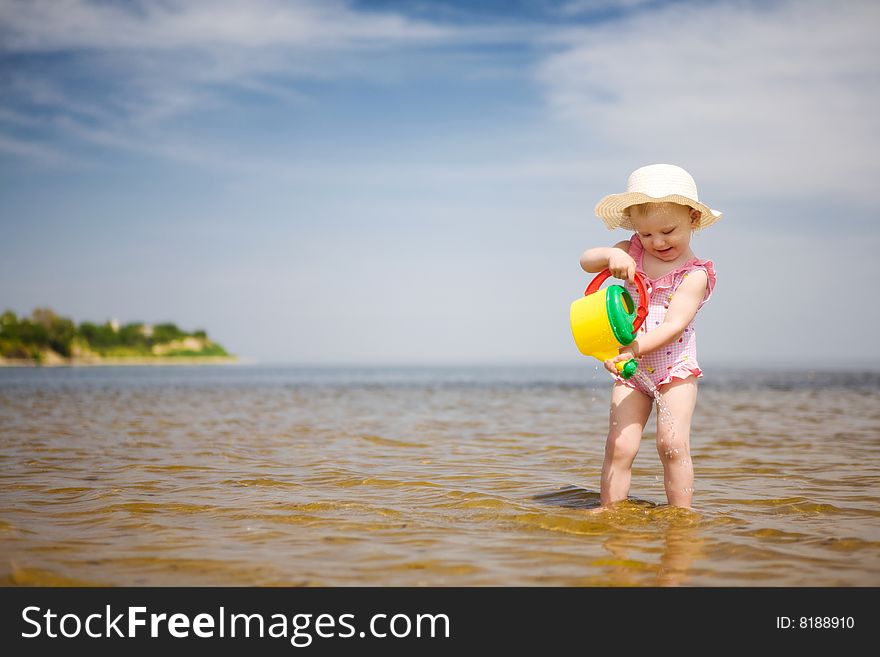 Small girl with watering-pot on the seashore