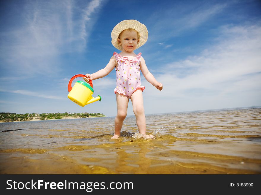 Small girl with watering-pot on the seashore